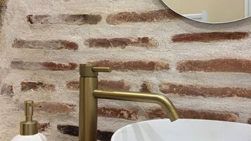 A bathroom with a white sink, brass faucet, and a soap dispenser.