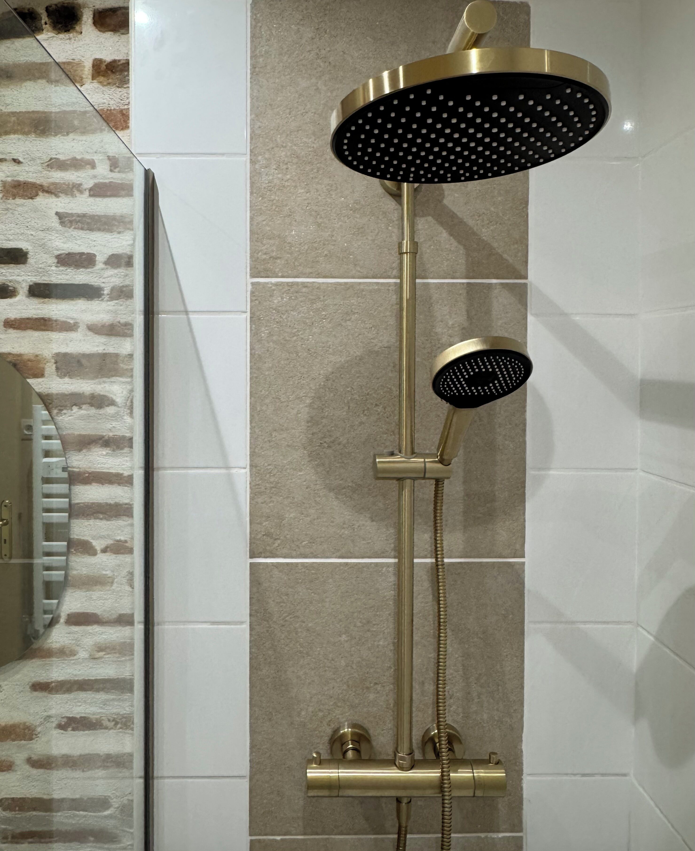 Una ducha moderna con detalles dorados, un cabezal de ducha de mano y un cabezal empotrado en la pared.