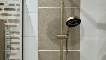 Una ducha moderna con detalles dorados, un cabezal de ducha de mano y un cabezal empotrado en la pared.