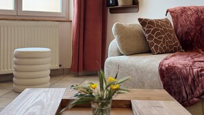 A living room with a sofa, a coffee table, a potted plant, and a window with curtains. - Cosy apartment on the banks of the Nivernais Canal (Saint-Léger-des-Vignes)