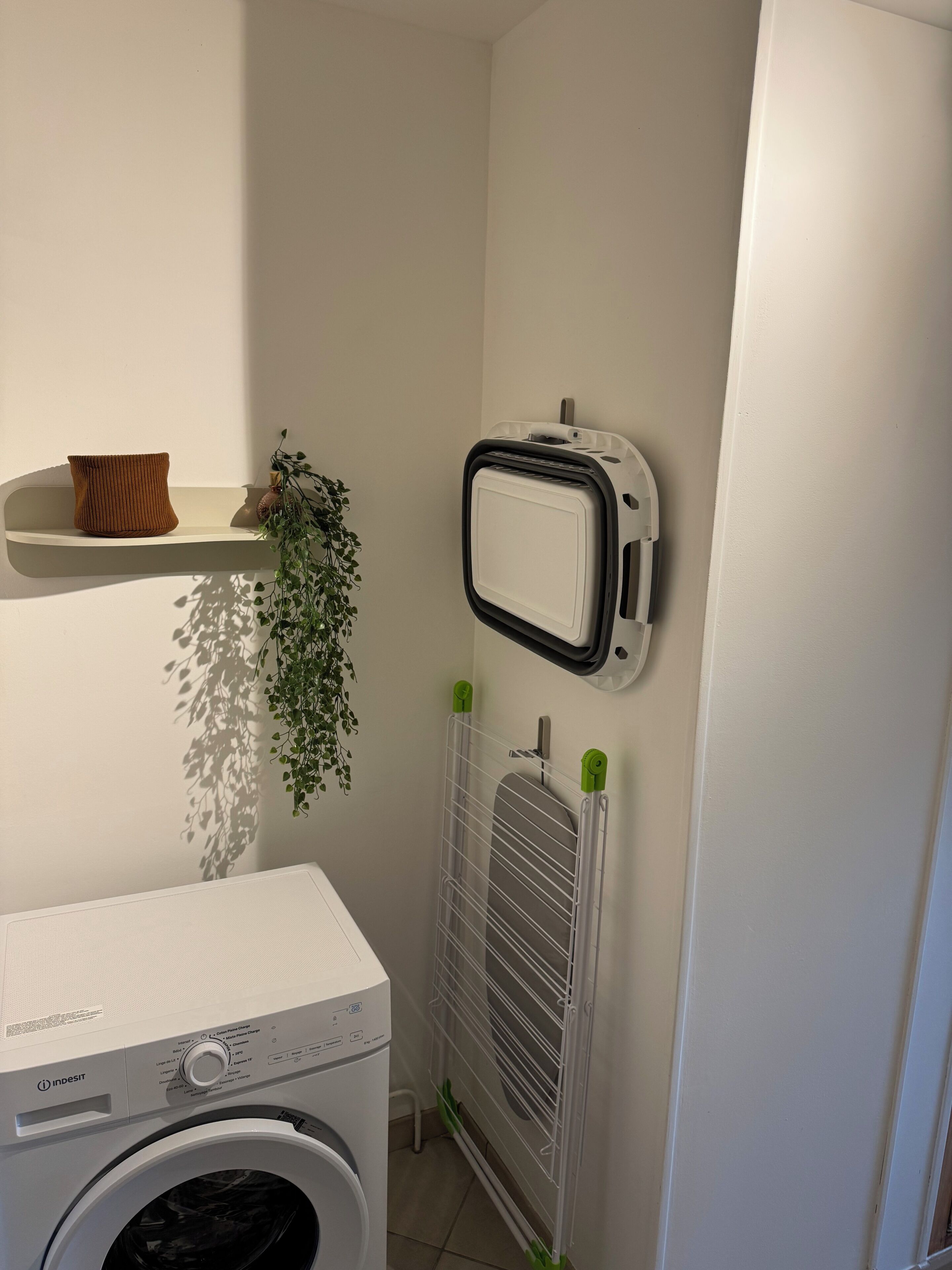 A laundry room with a washing machine, a radiator, and a shelf with a plant.