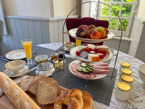 A breakfast setting with bread, fruit, cheese, and meats on a table. - Château de Planquery (Planquery)