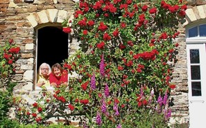 A stone building with a window and a door, surrounded by red and purple flowers. - Château de Planquery (Planquery)