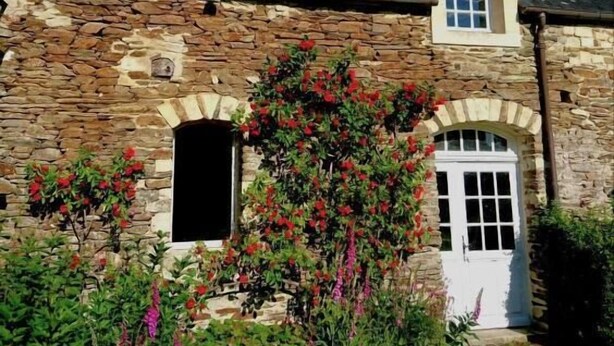 Un edificio de piedra con una puerta blanca, una ventana pequeña y un jardín lleno de flores.