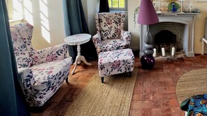 A room with a fireplace, floral armchairs, a round table, and a patterned rug. - Château de Planquery (Planquery)