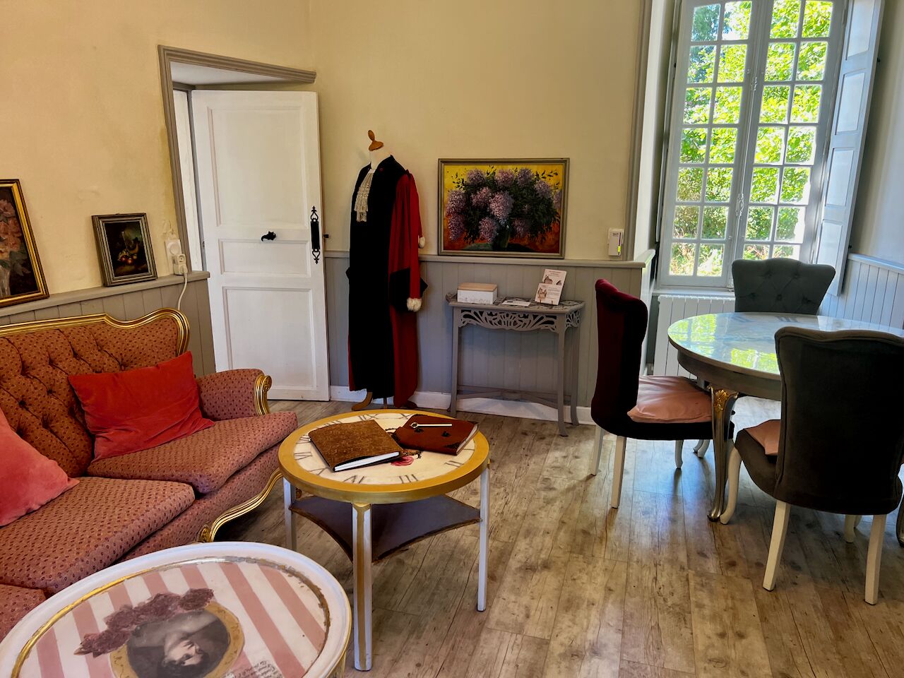 A living room with a sofa, a round table, a chair, a door, and a window with a view of trees.