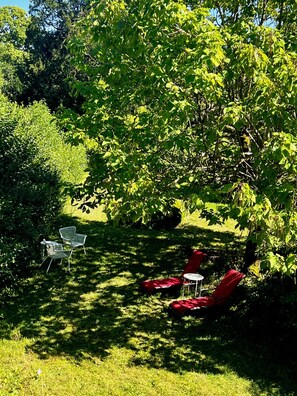 A garden with a tree, two white chairs, and two red lounge chairs.