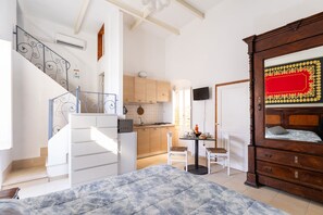 Um quarto com uma cama, cômoda de madeira, mesa de jantar com cadeiras, cozinha e escada.