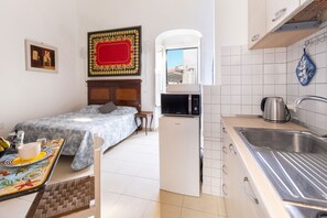 Una camera compatta con un letto, un angolo cottura, un'area pranzo e vista attraverso un arco.
