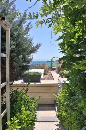 A garden pathway leading to a terrace with potted plants and a view of the sea.