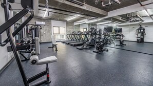 Een fitnessruimte met diverse trainingsapparaten, een grote spiegel en een betonnen plafond.