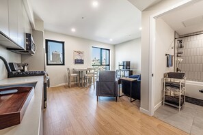 Una cocina moderna con zona de comedor, un sillón gris y vistas a la ciudad a través de un amplio ventanal.