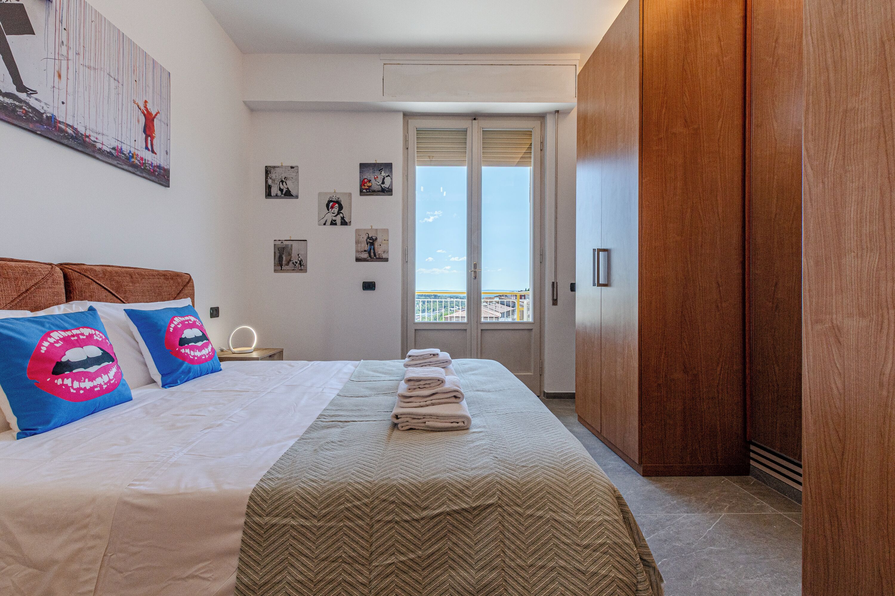 A hotel room with a bed, a wardrobe, a balcony, and a view of the city.