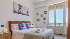 Ein Schlafzimmer mit Bett, Nachttisch, Spiegel, Fenster mit Blick und einer Tür.