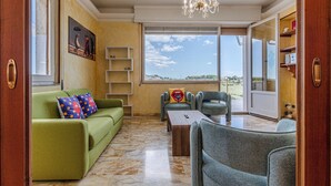 Ein geräumiges Wohnzimmer mit einem grünen Sofa, einem grauen Sessel, einem Holztisch und einem großen Fenster mit Blick ins Freie.