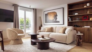 A living room with a sofa, a round coffee table, a chair, a bookshelf, and a large framed artwork. - A UNIQUE BLEND OF HISTORY, CULTURE, FASHION & GASTRONOMY – LE MARAIS (Paris)