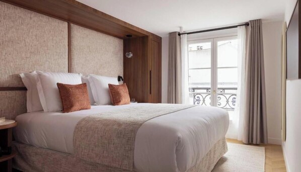 A hotel room with a large bed, a wooden headboard, a nightstand, and a balcony with a railing. - A UNIQUE BLEND OF HISTORY, CULTURE, FASHION & GASTRONOMY – LE MARAIS (Paris)