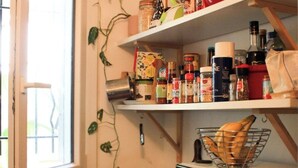 Een keuken met planken vol diverse etenswaren, een magnetron en een raam met planten.