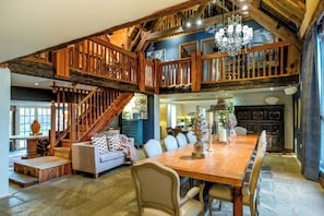 A spacious dining area with a wooden table and chairs, a staircase leading to an upper level, and a chandelier. - The Subedge Collection - A Unique Cotswolds Escape (Weston Subedge)