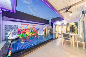 Un área de piscina interior moderna con un mural colorido, un tobogán y una zona de estar con vistas a la piscina.