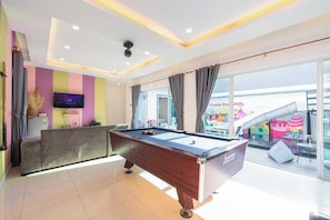 A modern room with a pool table, a flat-screen TV, and a balcony with a view of a colorful playground.