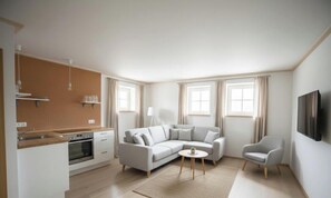 Una sala de estar moderna con un sofá, una silla, una mesita, un televisor y una cocina con un fregadero y armarios.