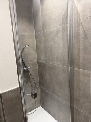 Ducha con puerta de vidrio, azulejos grises y cabezal de ducha cromado.