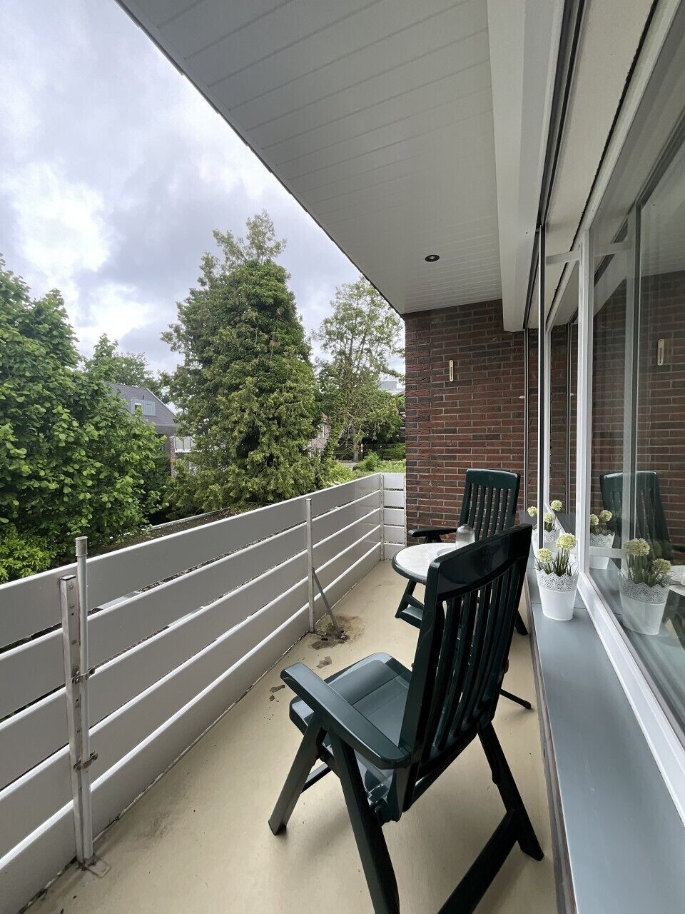 A balcony with a metal railing, a table, two chairs, and a potted plant.