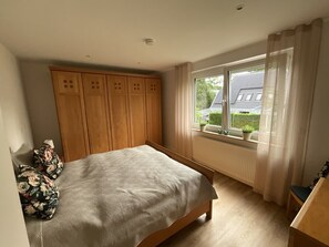 A bedroom with a bed, wooden wardrobe, window with curtains, and a view of the outside.