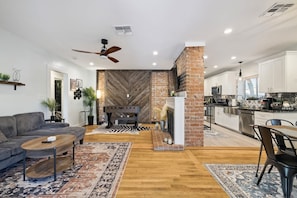 A modern living room with a fireplace, a dining area, and a kitchen. - The Glow-Up House | Pool, Spa & Glam Room (Phoenix)