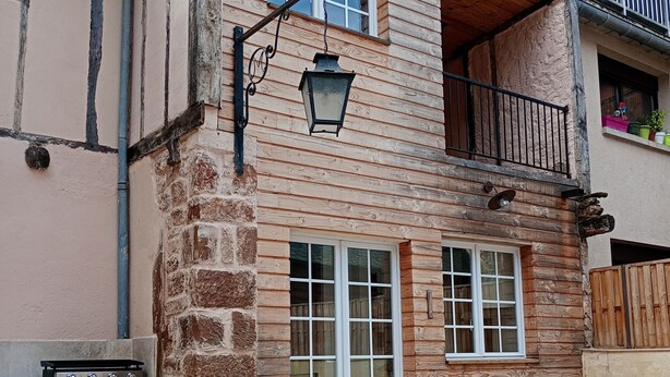 A wooden building with a balcony, a table, and a grill. - Gite Le Mansois (Marcillac-Vallon)
