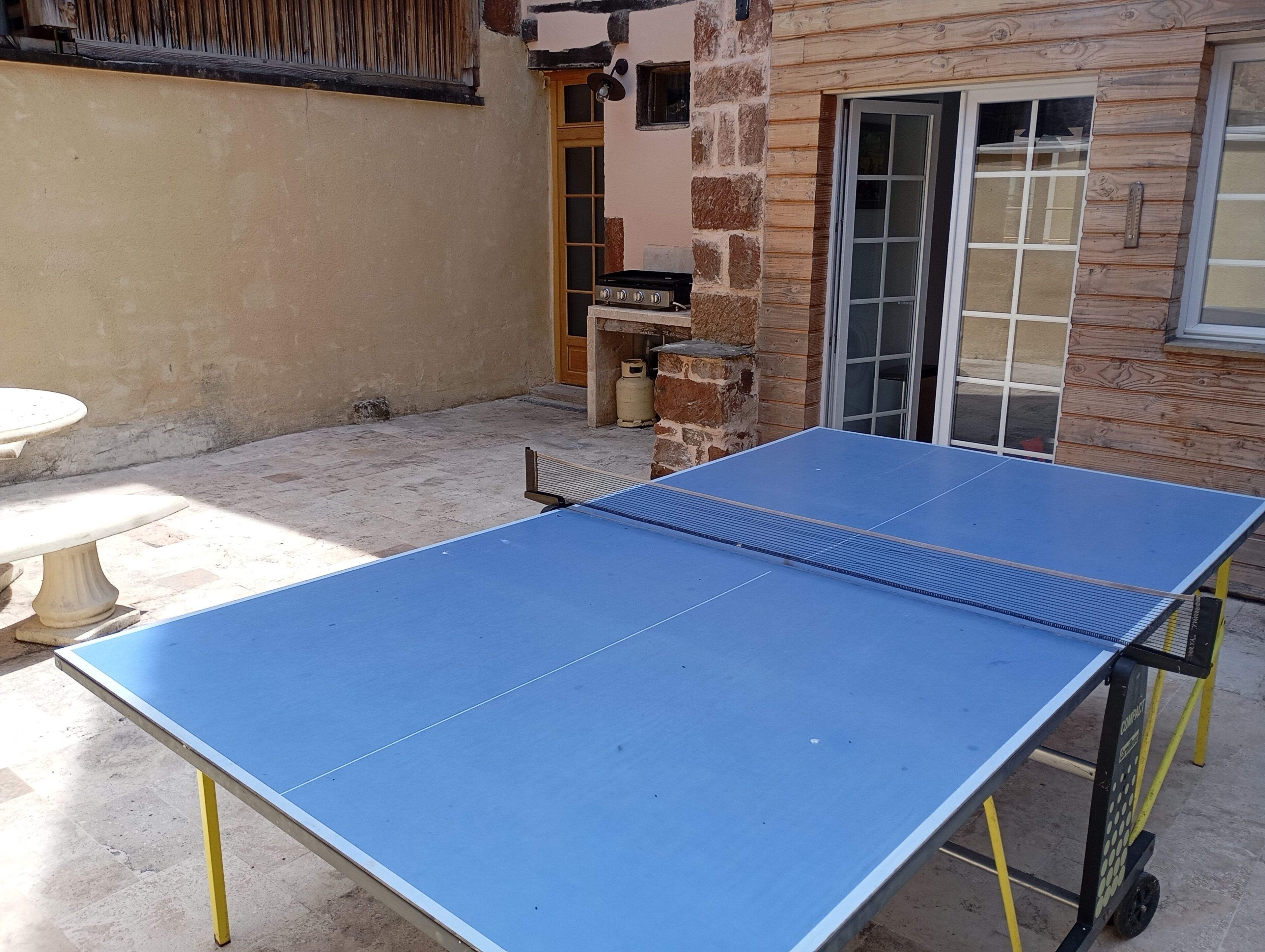 A blue ping pong table in an outdoor area with a stone wall and a wooden door.