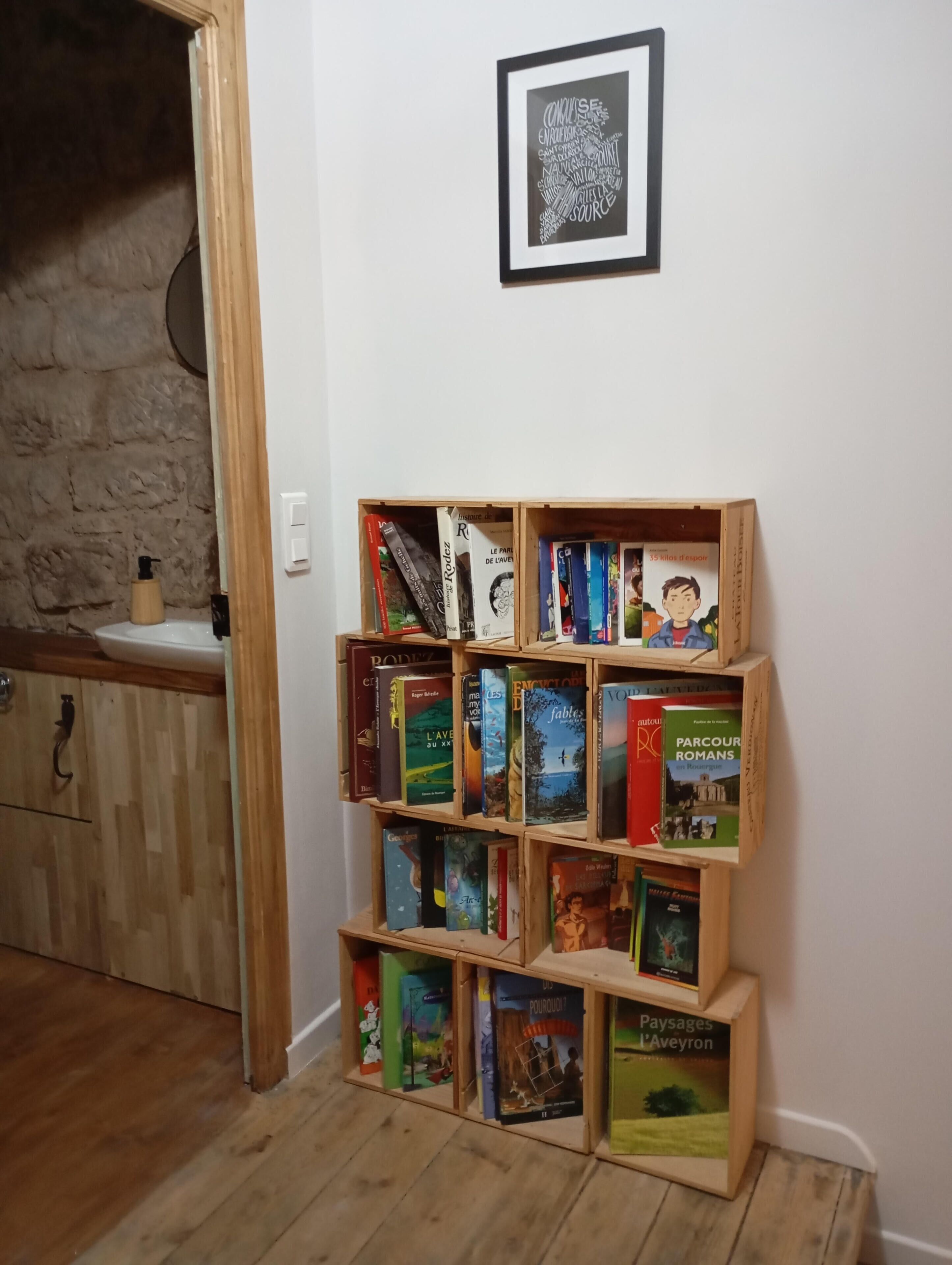 A bookshelf with books, a framed word cloud on the wall, and a stone wall in the background.
