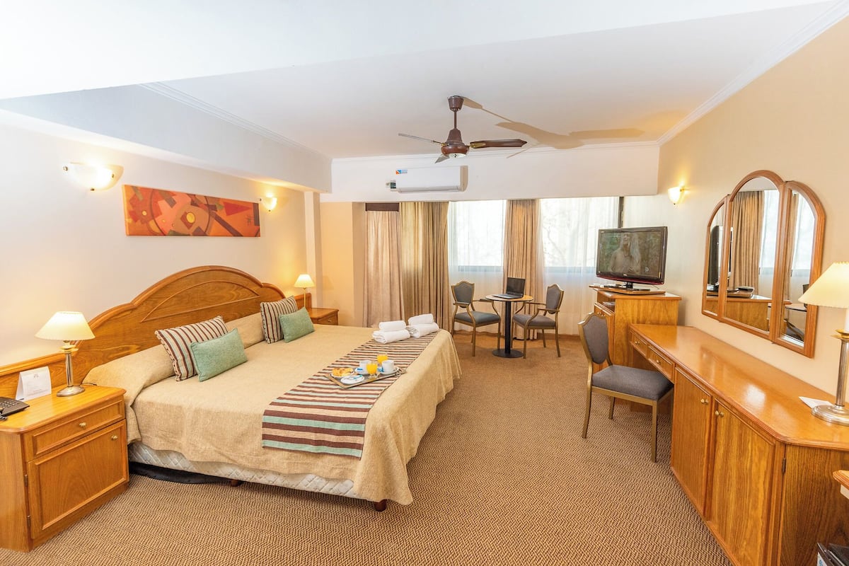 A hotel room with a bed, desk, television, and a ceiling fan.