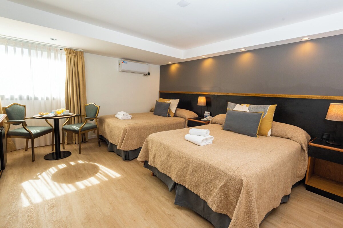 Une chambre d’hôtel avec deux lits, un coin repas et une fenêtre avec des rideaux.