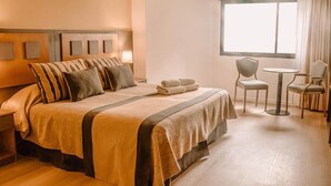 A hotel room with a large bed, two chairs, a small table, and a window. - Hotel Tronador (Mar del Plata)