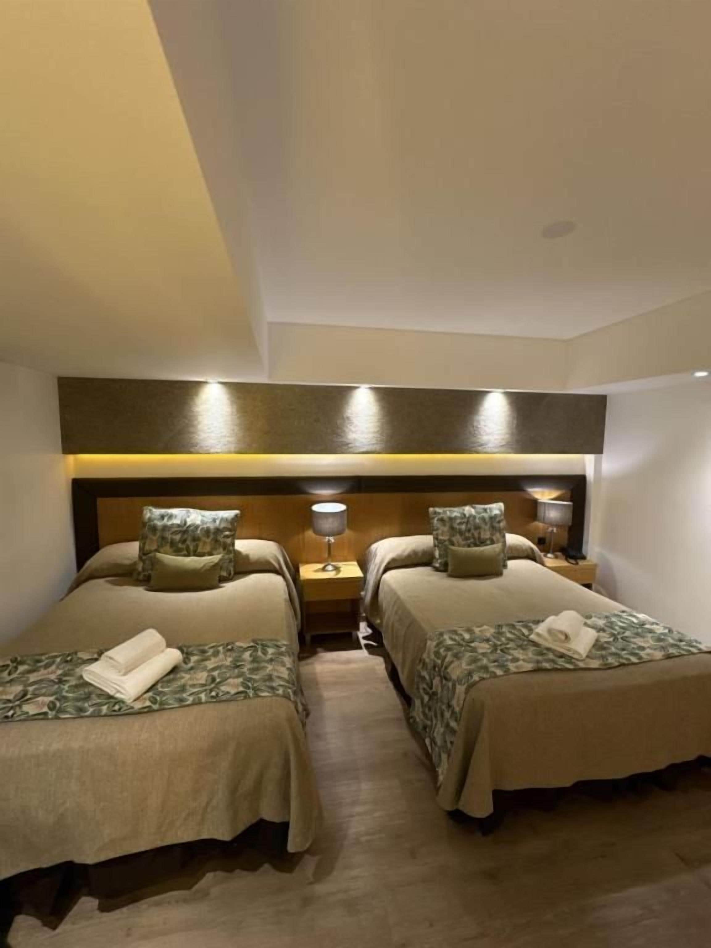 A hotel room with two single beds, a wooden headboard, bedside lamps, and a small nightstand.