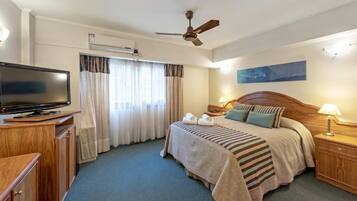 Une chambre d’hôtel avec un lit, une télévision, un ventilateur de plafond, une table de chevet, une lampe et un tableau au mur.