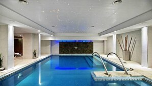 A large indoor swimming pool with clear blue water, a dark wall at the far end, and a ceiling with recessed lighting. - Hotel Tronador (Mar del Plata)