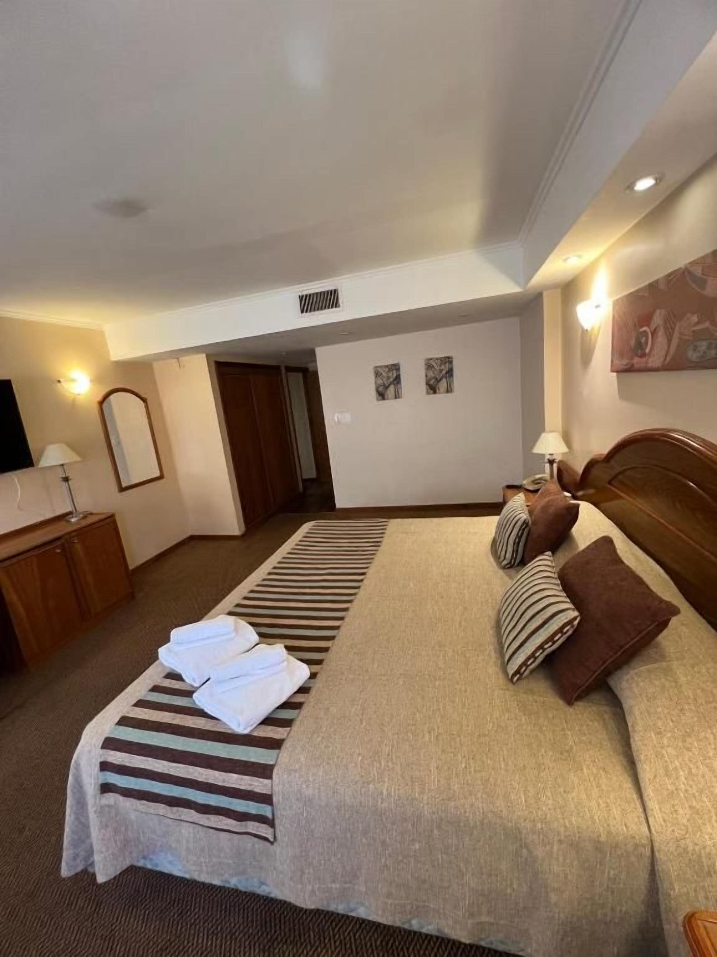 Une chambre d’hôtel avec un grand lit, une table de chevet, une lampe et une porte donnant sur une autre pièce.