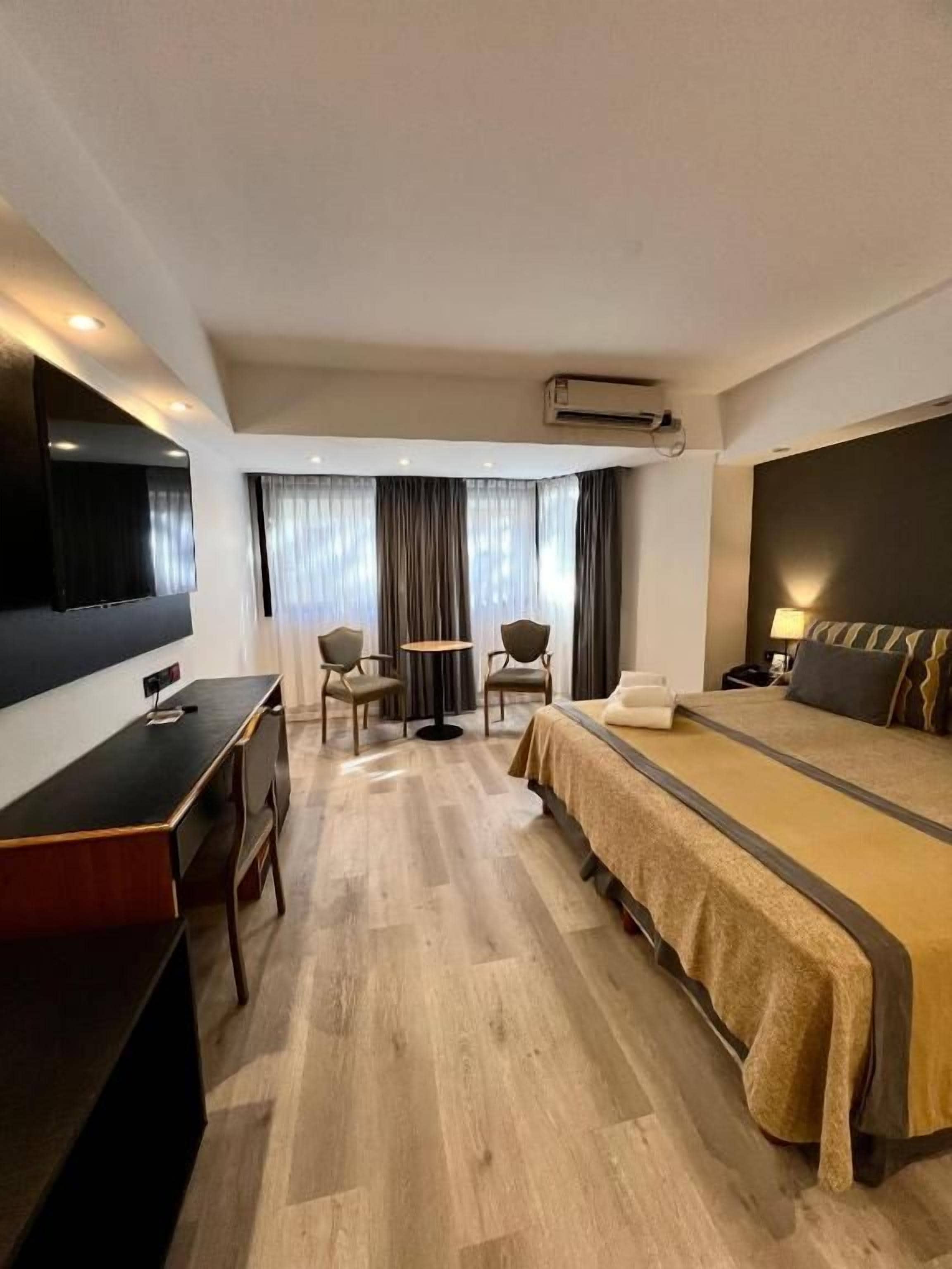 Habitación de hotel con cama, escritorio, silla, televisor y aire acondicionado.