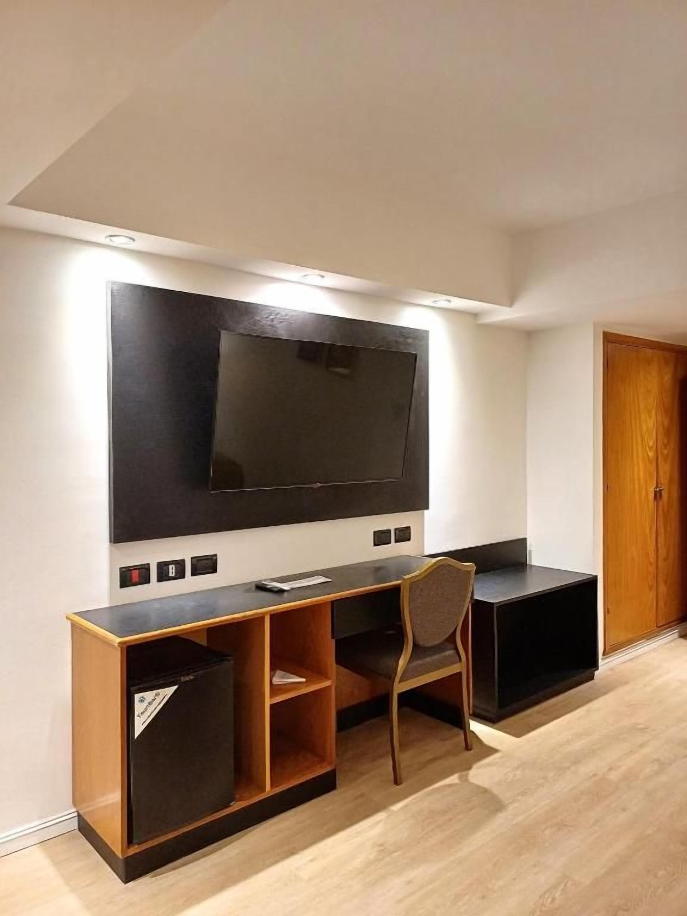 A modern living room with a large flat-screen TV mounted on the wall, a wooden entertainment unit, and a single chair.