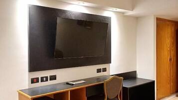 A modern living room with a large flat-screen TV mounted on the wall, a wooden entertainment unit, and a single chair.