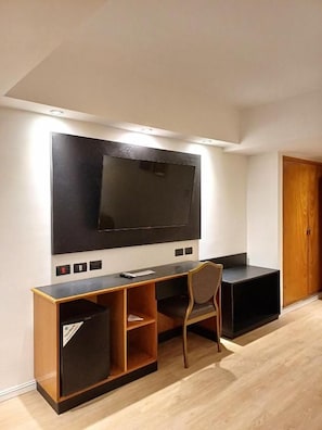 A modern living room with a large flat-screen TV mounted on the wall, a wooden entertainment unit, and a single chair. - Hotel Tronador (Mar del Plata)