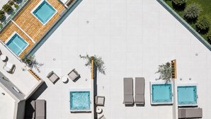An aerial view of a rooftop with multiple swimming pools, lounge chairs, and potted plants.