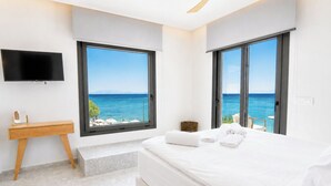 A modern hotel room with a large bed, a desk, a TV, and a view of the sea.