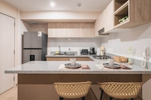A modern kitchen with a granite countertop, two woven chairs, a built-in oven, and a refrigerator. - 2 bedrooms with A/C, 2 bathrooms, desk, pool in Larco (Miraflores)