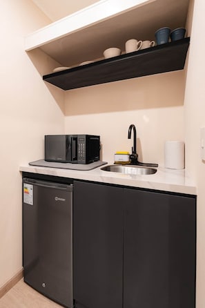 A compact kitchen with a microwave, dishwasher, and a shelf above the sink. - Bright Studio w/ View · A/C · Pool · 24/7 Doorman (Miraflores)