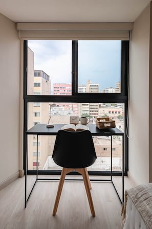 A room with a large window, a desk, a chair, and a view of buildings. - Studio with AC, desk, view and pool in Larco (Miraflores)