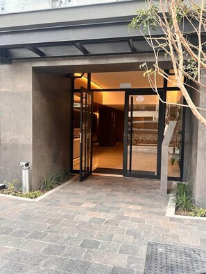 A building entrance with a glass door, a metal staircase, and a small garden area. - Bright Studio w/ View · A/C · Pool · 24/7 Doorman (Miraflores)
